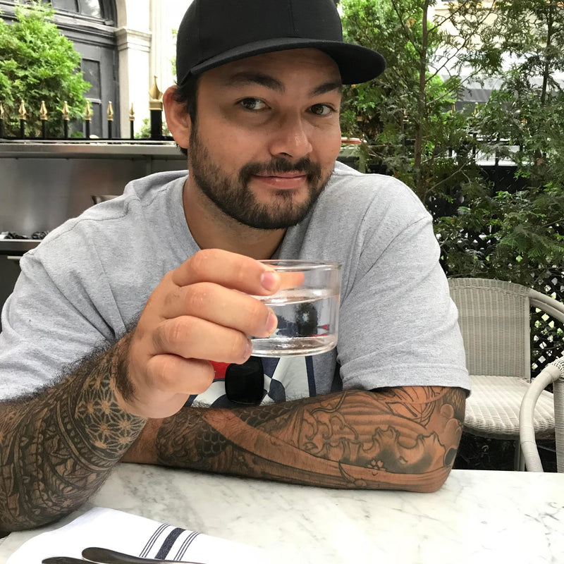 Man with tattoos holding a glass of water outdoors