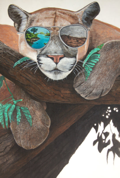 Puma wearing sunglasses with a scenic reflection, perched on a branch.